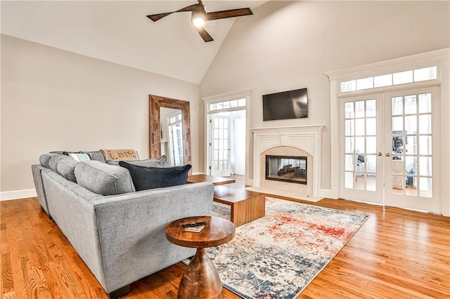 living room featuring high vaulted ceiling, wood finished floors, a fireplace, baseboards, and ceiling fan