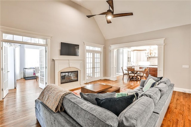 living area with french doors, light wood finished floors, a high end fireplace, and ceiling fan with notable chandelier