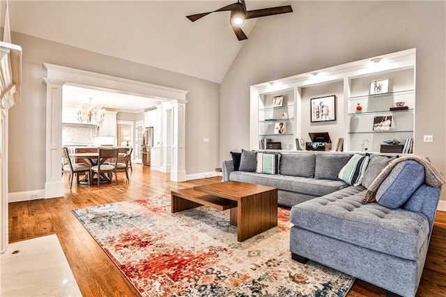 living area featuring ceiling fan with notable chandelier, high vaulted ceiling, light wood-style floors, and decorative columns