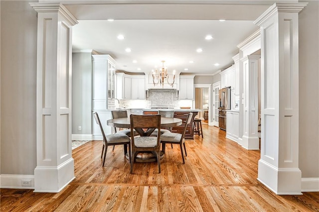 dining space featuring a notable chandelier, light wood-style flooring, ornamental molding, and ornate columns