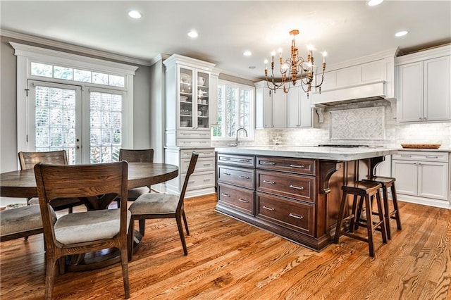 kitchen with dark brown cabinets, crown molding, a breakfast bar, light wood-style floors, and an inviting chandelier