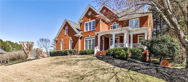 view of front facade featuring brick siding, covered porch, and a front yard