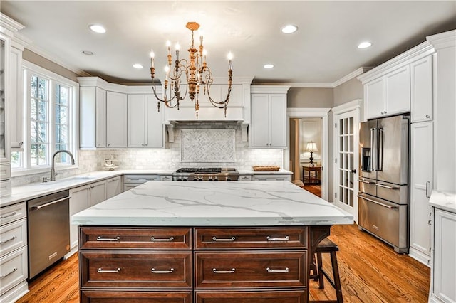 kitchen with a notable chandelier, a sink, appliances with stainless steel finishes, crown molding, and dark brown cabinets