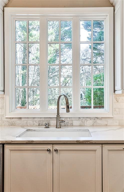 kitchen featuring a sink, light stone countertops, backsplash, and white cabinets