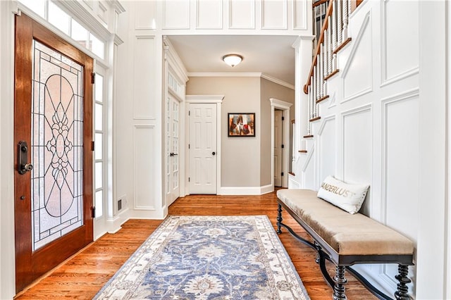 entrance foyer featuring stairway, baseboards, light wood-style flooring, ornamental molding, and a decorative wall