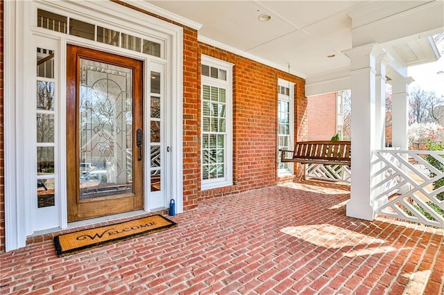 doorway to property featuring a porch and brick siding