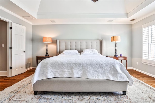 bedroom featuring visible vents, ornamental molding, a tray ceiling, and wood finished floors