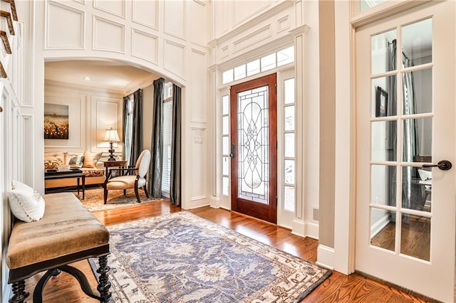 foyer featuring arched walkways, light wood-style floors, plenty of natural light, and a decorative wall