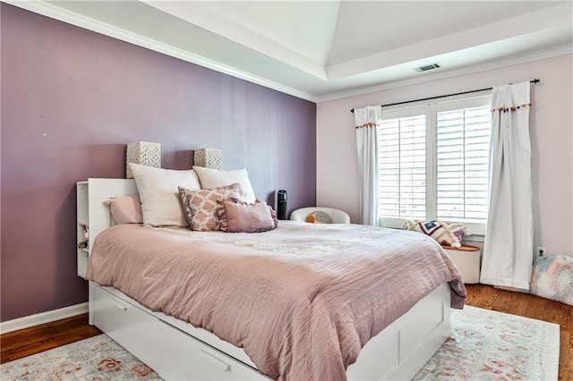 bedroom with visible vents, baseboards, wood finished floors, and crown molding