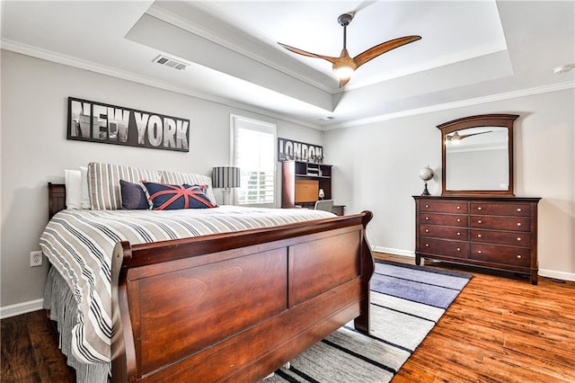 bedroom with a tray ceiling, wood finished floors, visible vents, and ornamental molding