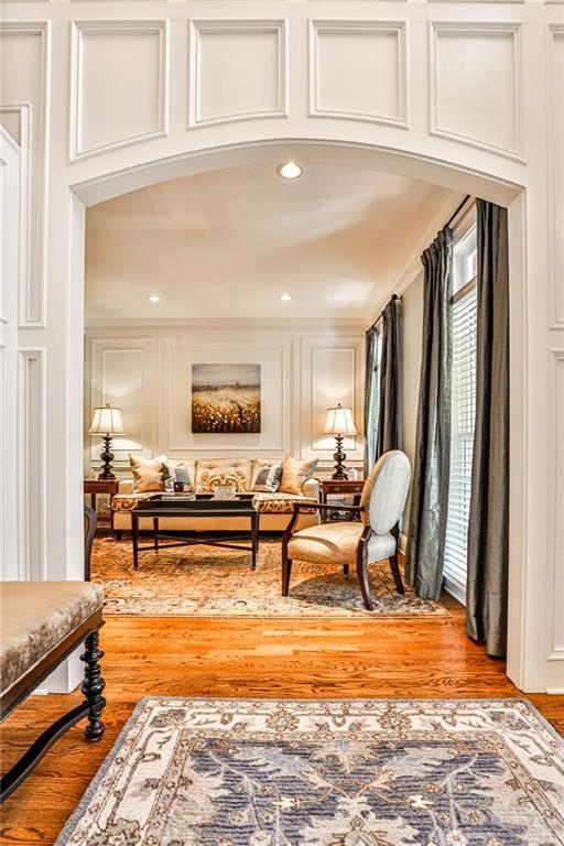 living area featuring arched walkways, a decorative wall, crown molding, and light wood-type flooring