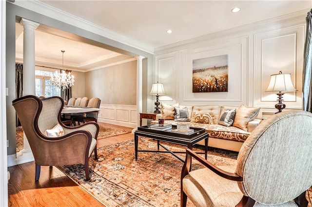 living area with an inviting chandelier, a decorative wall, wood finished floors, and ornate columns