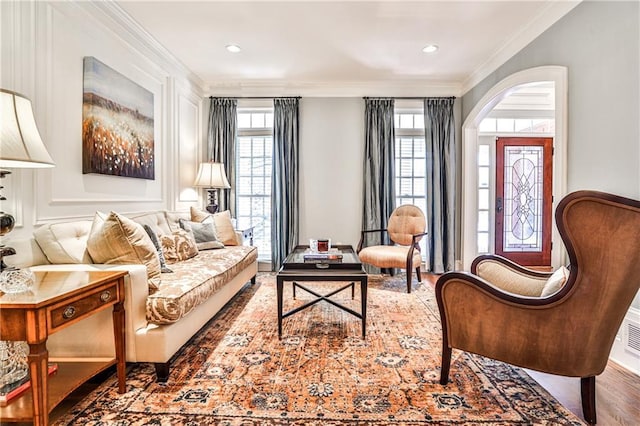 sitting room with arched walkways, a healthy amount of sunlight, crown molding, and wood finished floors