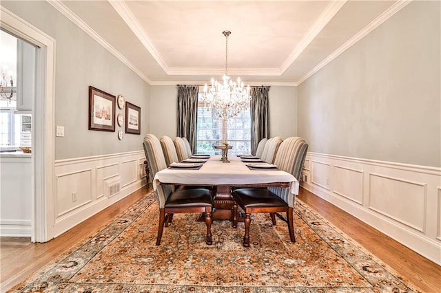 dining area with visible vents, a raised ceiling, a notable chandelier, and wood finished floors