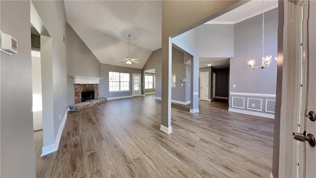 unfurnished living room with wood finished floors, a textured ceiling, a fireplace with raised hearth, and ceiling fan with notable chandelier