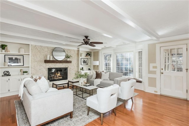 living room with beamed ceiling, a fireplace, light hardwood / wood-style floors, and built in shelves