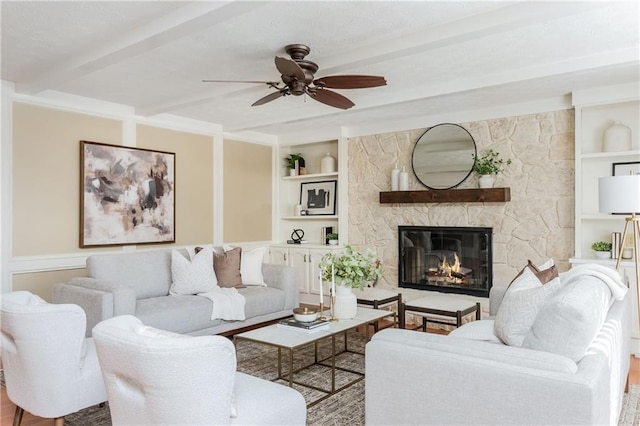 living room featuring beam ceiling, a fireplace, built in features, and ceiling fan