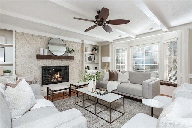 living room with beamed ceiling, ceiling fan, a fireplace, and built in shelves