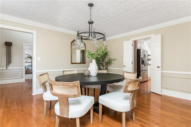 dining space with a notable chandelier, crown molding, a textured ceiling, and light wood-type flooring