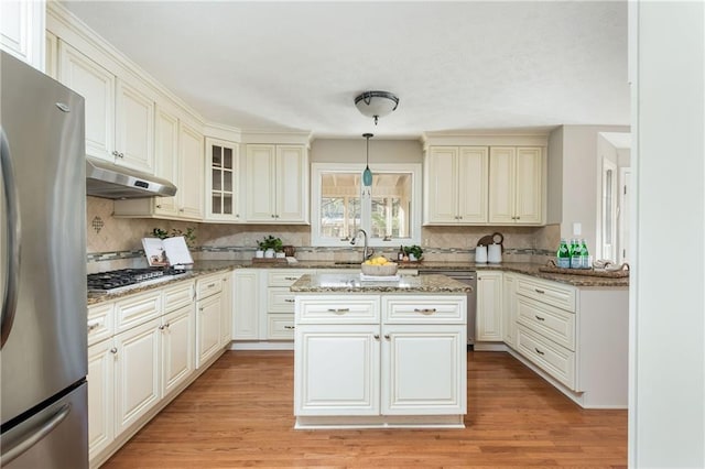 kitchen with stainless steel appliances, light hardwood / wood-style flooring, dark stone countertops, and decorative light fixtures