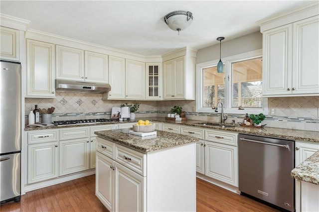 kitchen with sink, appliances with stainless steel finishes, hanging light fixtures, light stone countertops, and a kitchen island