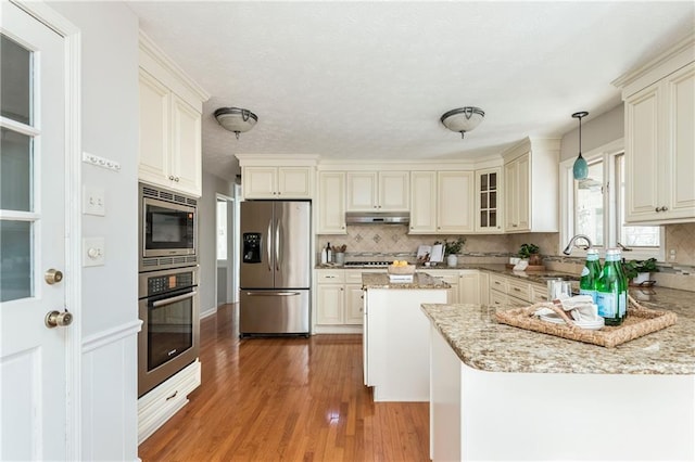 kitchen with hanging light fixtures, hardwood / wood-style floors, stainless steel appliances, light stone counters, and tasteful backsplash