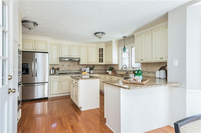 kitchen with appliances with stainless steel finishes, hanging light fixtures, light stone counters, kitchen peninsula, and cream cabinets