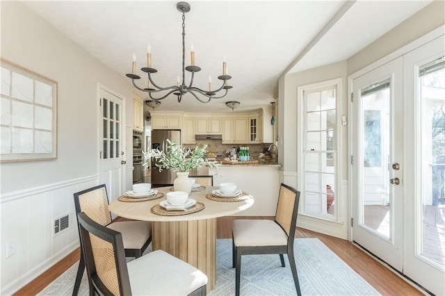 dining space with a notable chandelier, light wood-type flooring, and french doors