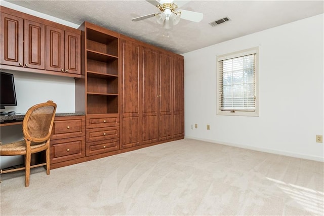 carpeted office space with ceiling fan, built in desk, and a textured ceiling