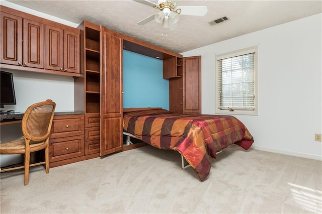 carpeted bedroom with ceiling fan, built in desk, and a textured ceiling