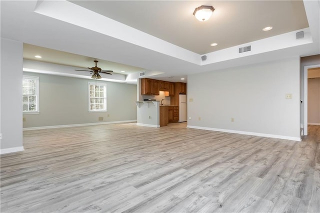 unfurnished living room with ceiling fan, a tray ceiling, and light wood-type flooring