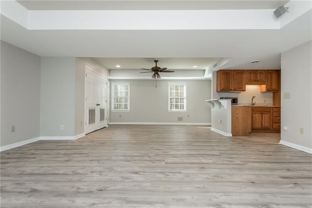 unfurnished living room featuring sink, a tray ceiling, light hardwood / wood-style floors, and ceiling fan