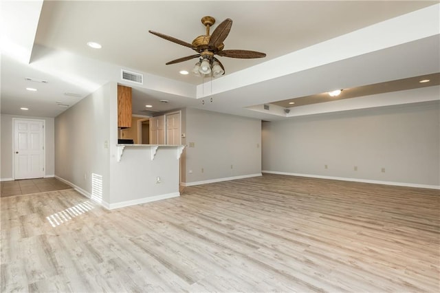 unfurnished living room featuring a raised ceiling, ceiling fan, and light wood-type flooring