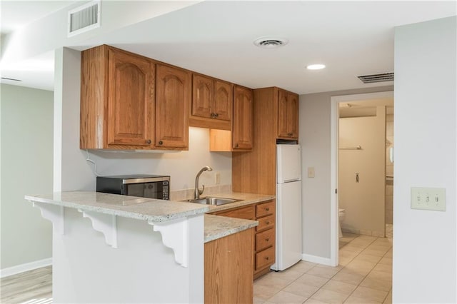 kitchen featuring sink, a breakfast bar area, white fridge, light stone counters, and kitchen peninsula