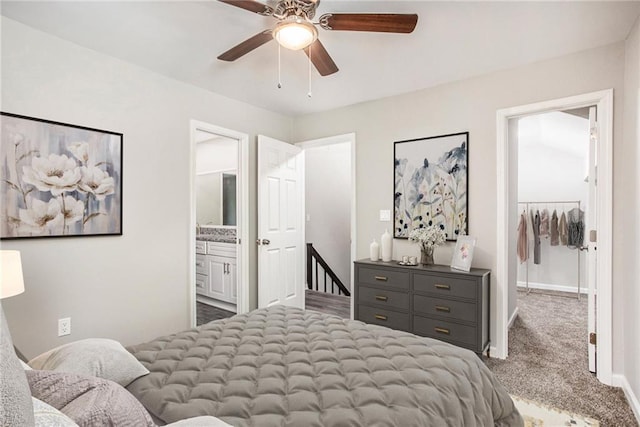 carpeted bedroom featuring a closet, ensuite bathroom, a walk in closet, and ceiling fan