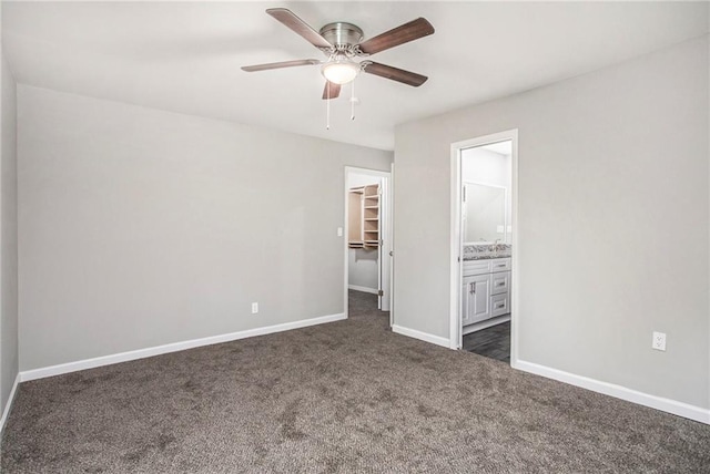 unfurnished bedroom with dark carpet, a walk in closet, a closet, and ceiling fan