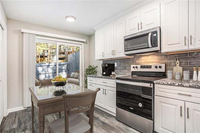 kitchen with appliances with stainless steel finishes, dark hardwood / wood-style floors, white cabinets, and tasteful backsplash