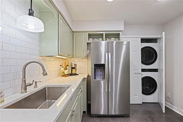 kitchen with sink, stacked washer and dryer, decorative backsplash, dark tile patterned floors, and stainless steel fridge with ice dispenser