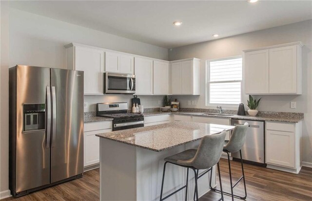 kitchen with dark hardwood / wood-style flooring, a kitchen island, white cabinetry, and appliances with stainless steel finishes