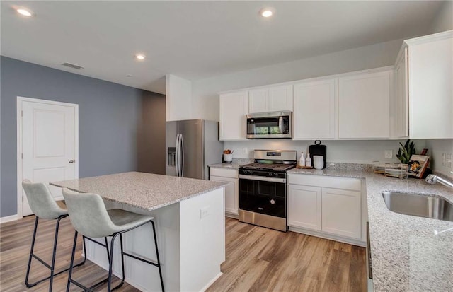 kitchen with stainless steel appliances, light stone counters, white cabinets, a kitchen island, and light wood-type flooring