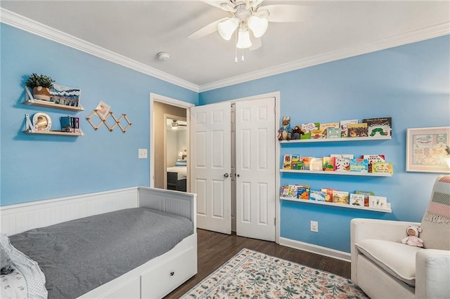 bedroom with dark wood finished floors, a closet, ornamental molding, wainscoting, and ceiling fan