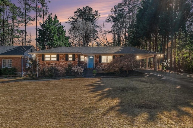 single story home with driveway, brick siding, an attached carport, and a yard