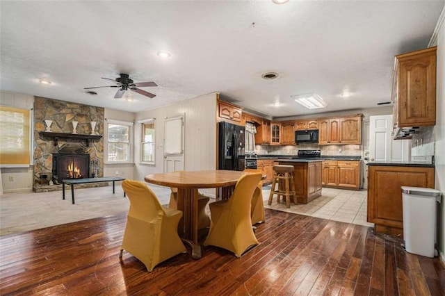 dining room featuring a stone fireplace, ceiling fan, and light hardwood / wood-style flooring