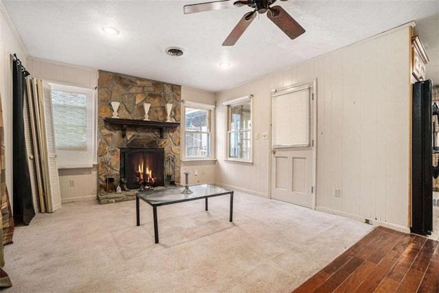 living room featuring a fireplace, light colored carpet, ceiling fan, and wooden walls