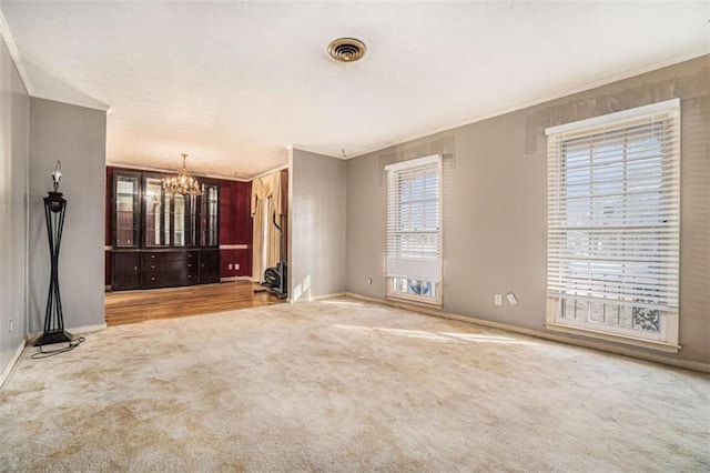 unfurnished living room featuring ornamental molding, light carpet, and an inviting chandelier