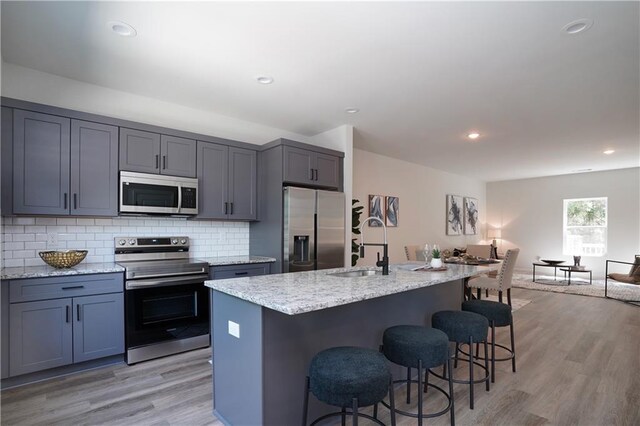 kitchen with a kitchen bar, light stone countertops, a sink, open floor plan, and stainless steel appliances