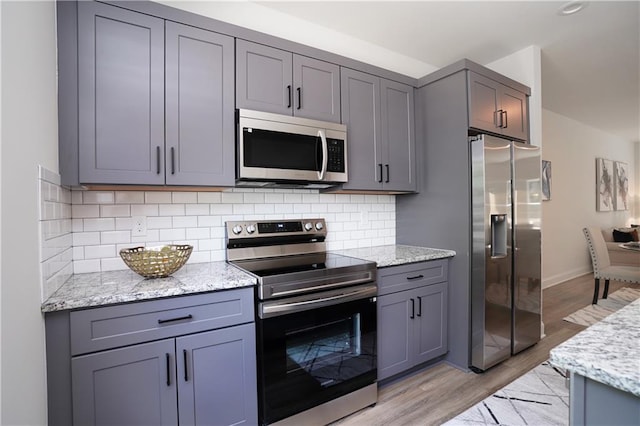 kitchen with light stone countertops, tasteful backsplash, gray cabinetry, and stainless steel appliances