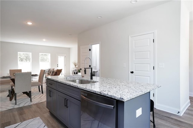 kitchen featuring a sink, light stone counters, stainless steel dishwasher, and wood finished floors