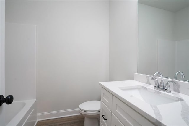 bathroom with vanity, wood finished floors, toilet, a washtub, and baseboards
