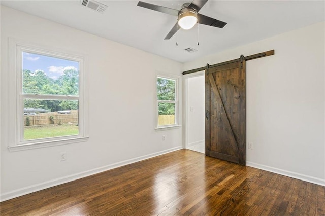 unfurnished room featuring ceiling fan, a healthy amount of sunlight, dark hardwood / wood-style flooring, and a barn door